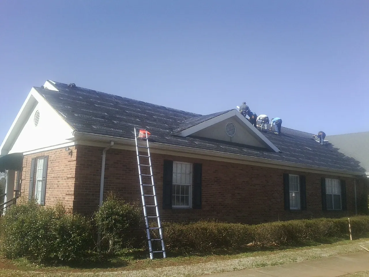Crew tearing shingles off a brick ranch roof with a ladder set — Metal Roof Repair work by our crew in Fairfield
